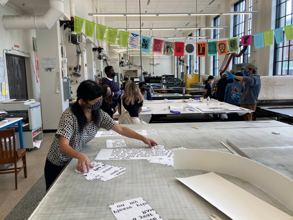 Artist working with papers in the foreground of large print shop with people working in the background