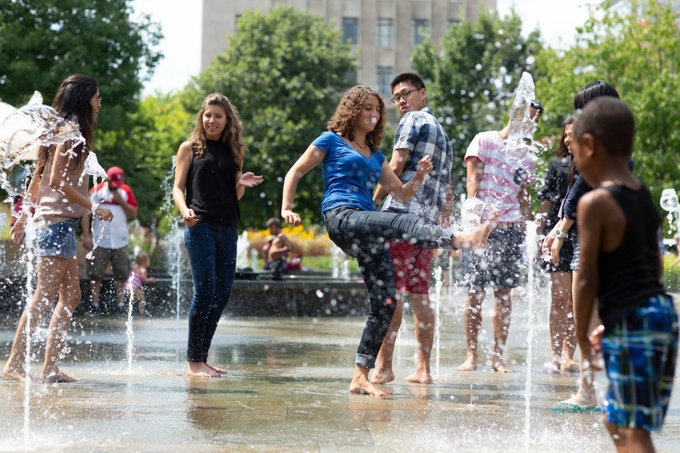 People playing in fountains in a city park.