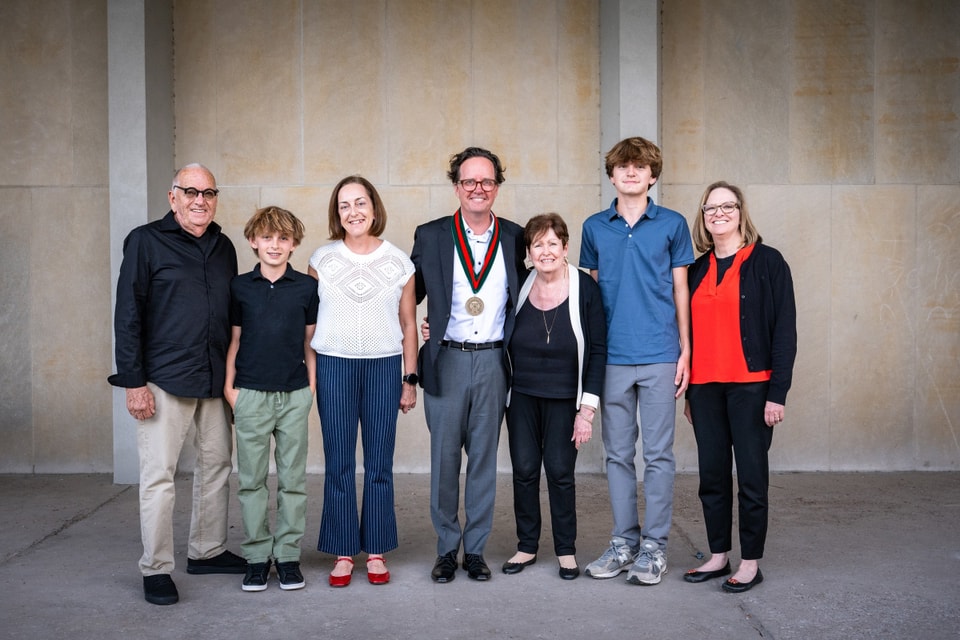 Seven people stand arm in arm and smile at the camera.