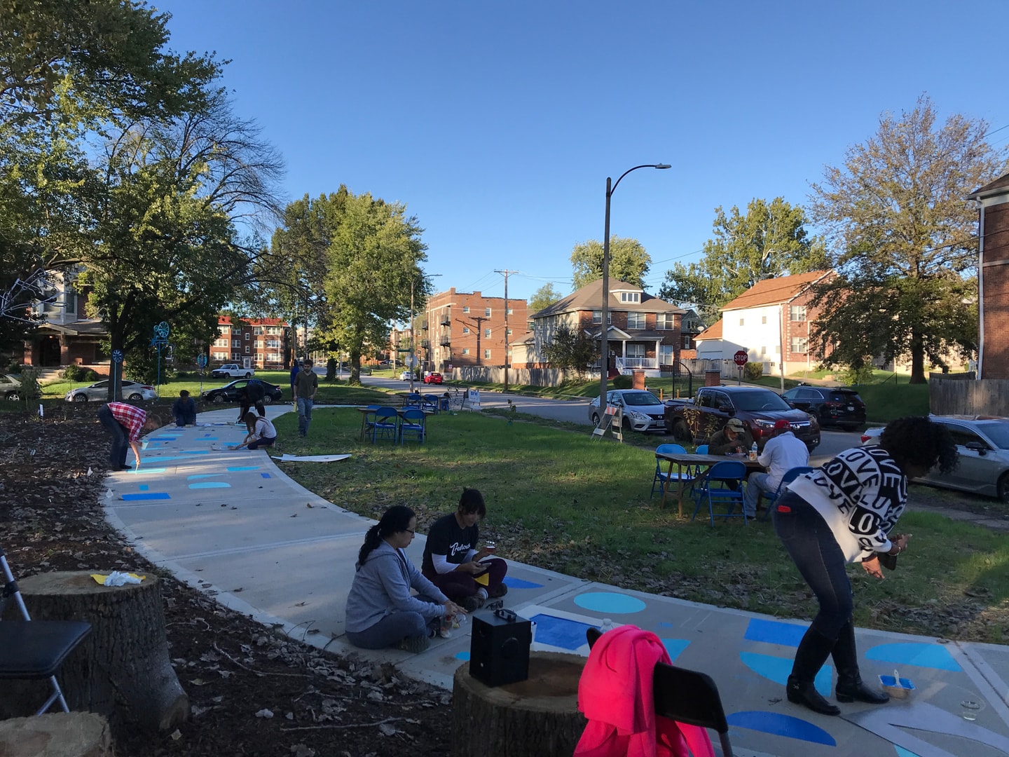 Groups of people painting geometric blue shapes on a curved pathway by a park