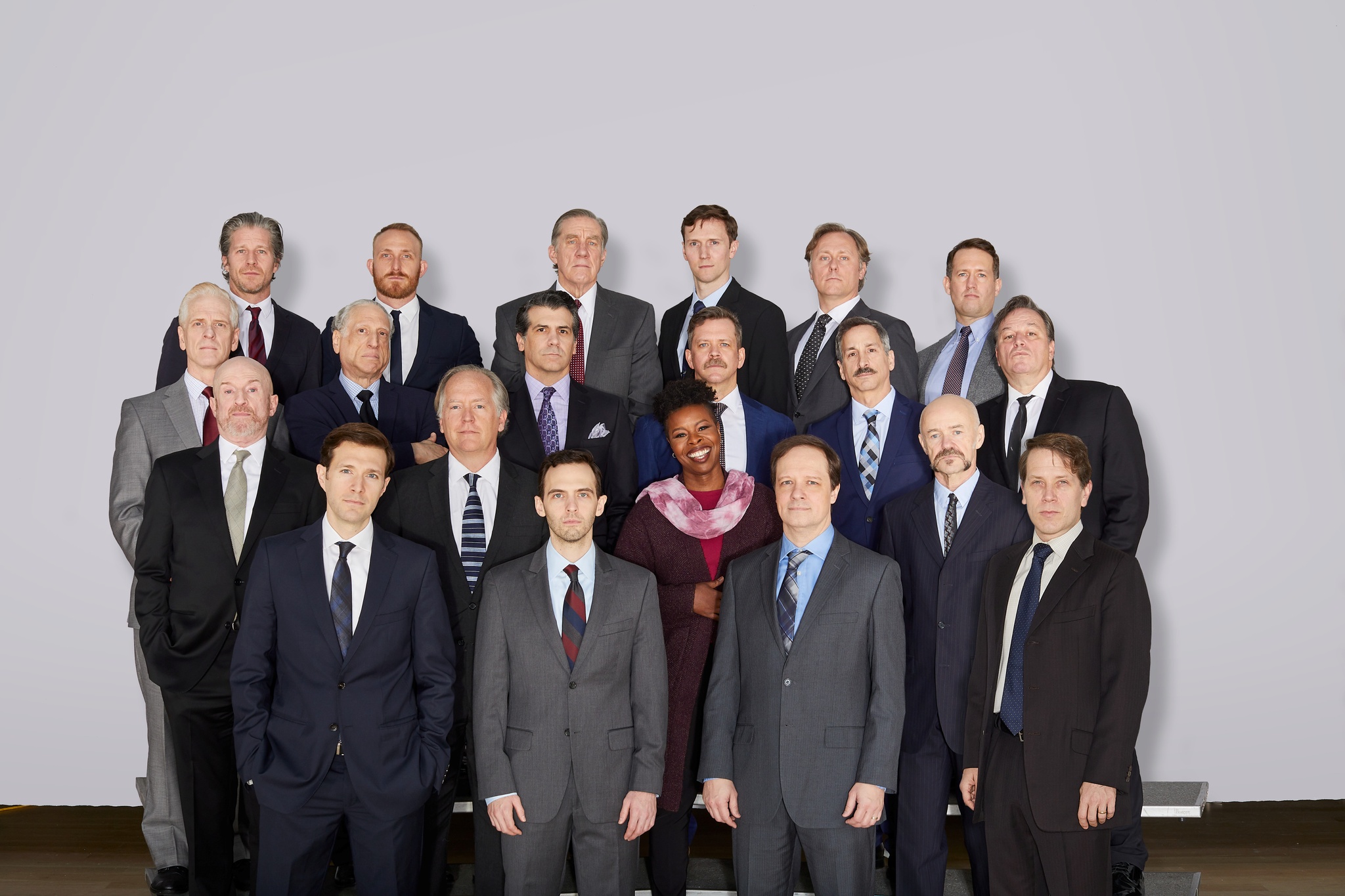A cast photo including 19 white men actors with a black woman actor arranged on risers as if in a school class photo