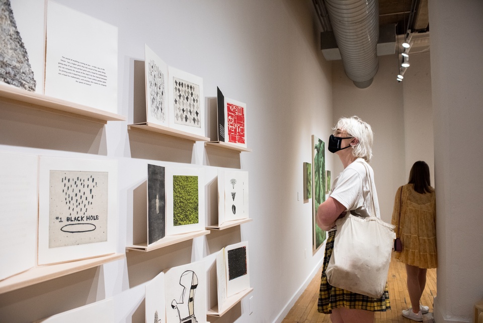 A gallery visitor observes print artworks displayed on a wall