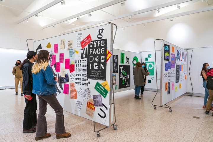 Wide shot of the gallery space of typography work filled with people. The event poster reads "Typeface Design," each letter set in a different novelty font.