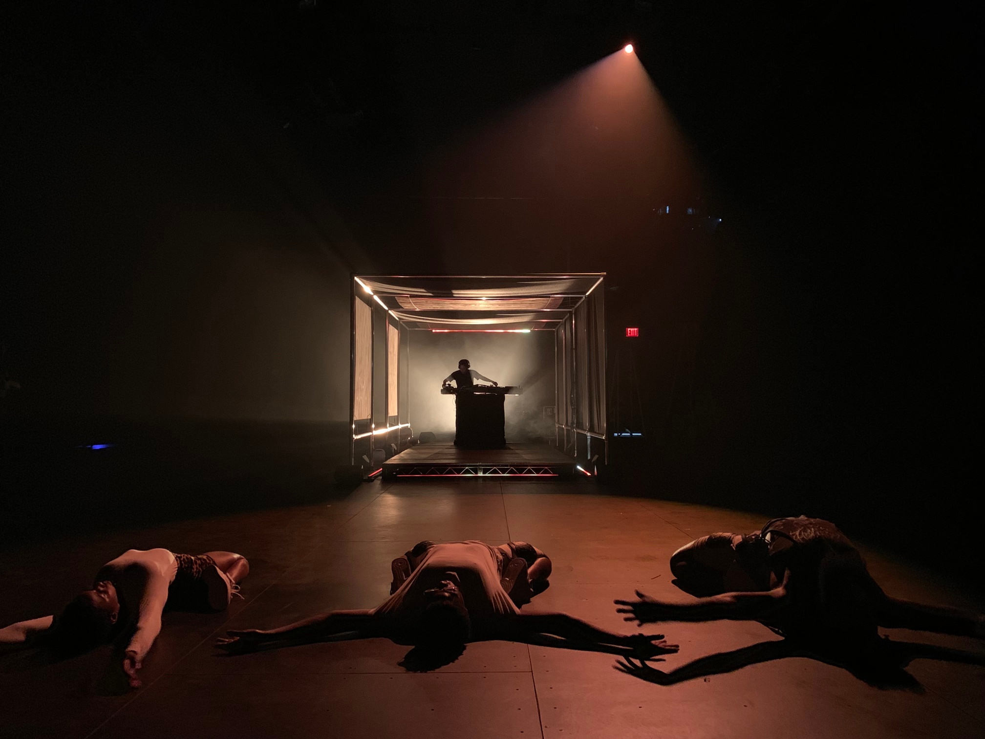 Dancers on a dramatically lit stage with DJ in the background.