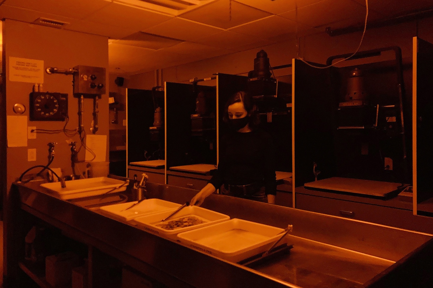 Photo of a student working in a photography darkroom; the photo has a deep orange tint to it.