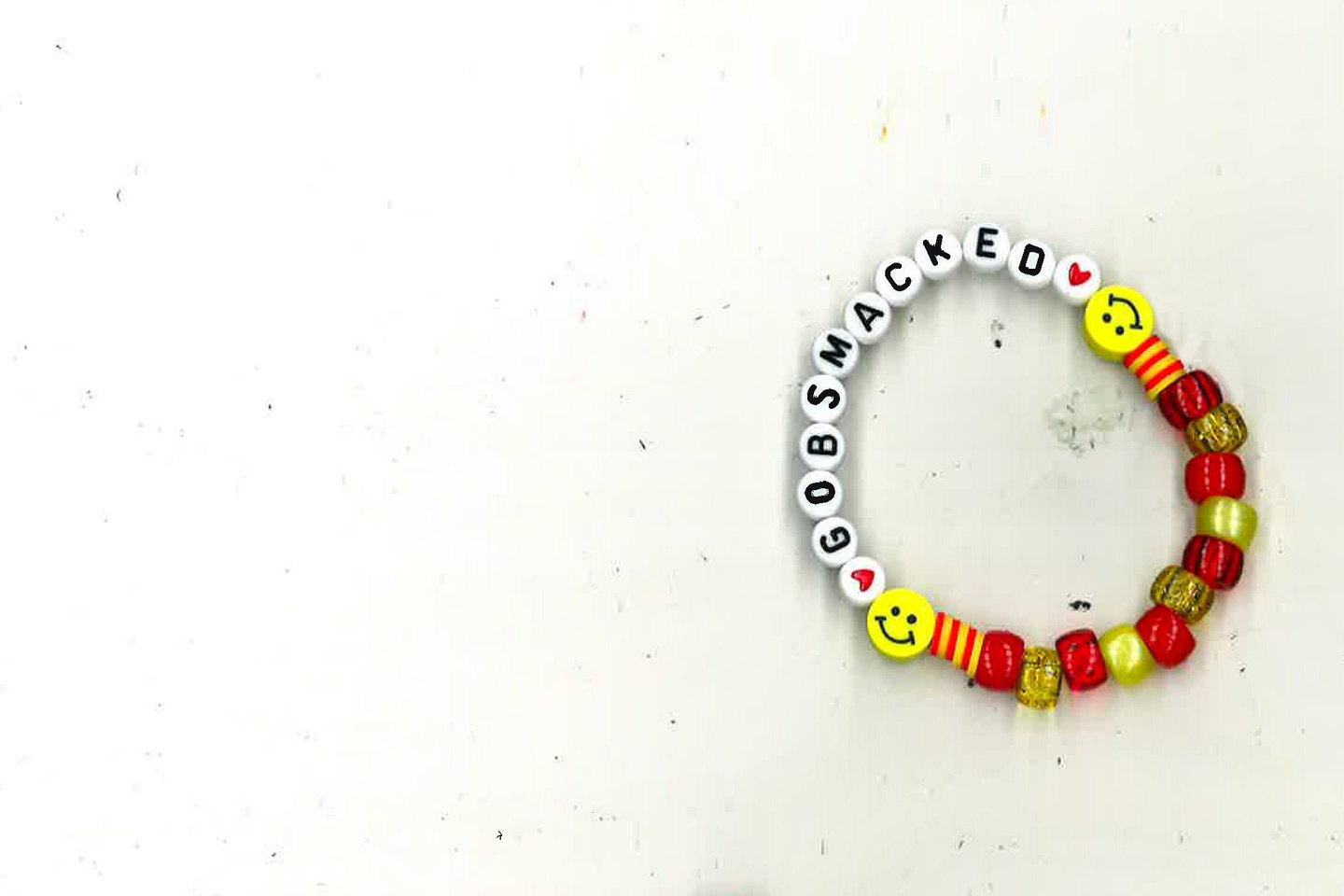Photo of a beaded bracelet, with red, yellow and clear beads on one side, two  yellow smiley-face beds, and then white beads with letters spelling the word GOBSMACKED.