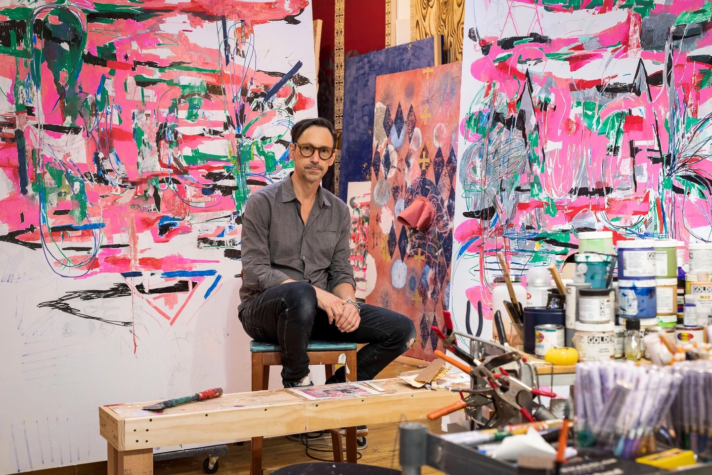 Portrait of Mark Fox in studio, with vibrant paintings on the walls behind him.