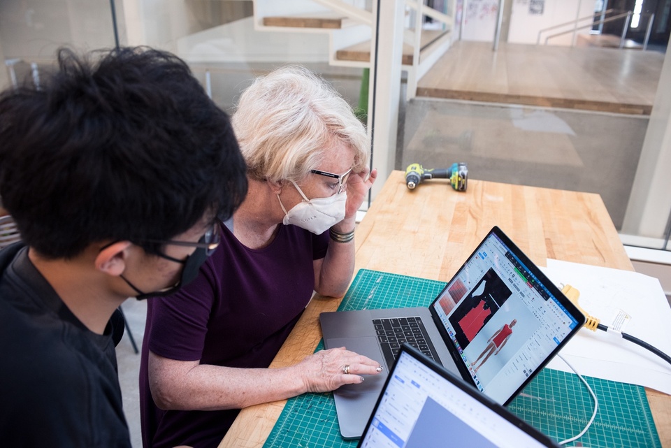 Instructor demonstrates a 3D clothing modeling software on a laptop to a student.