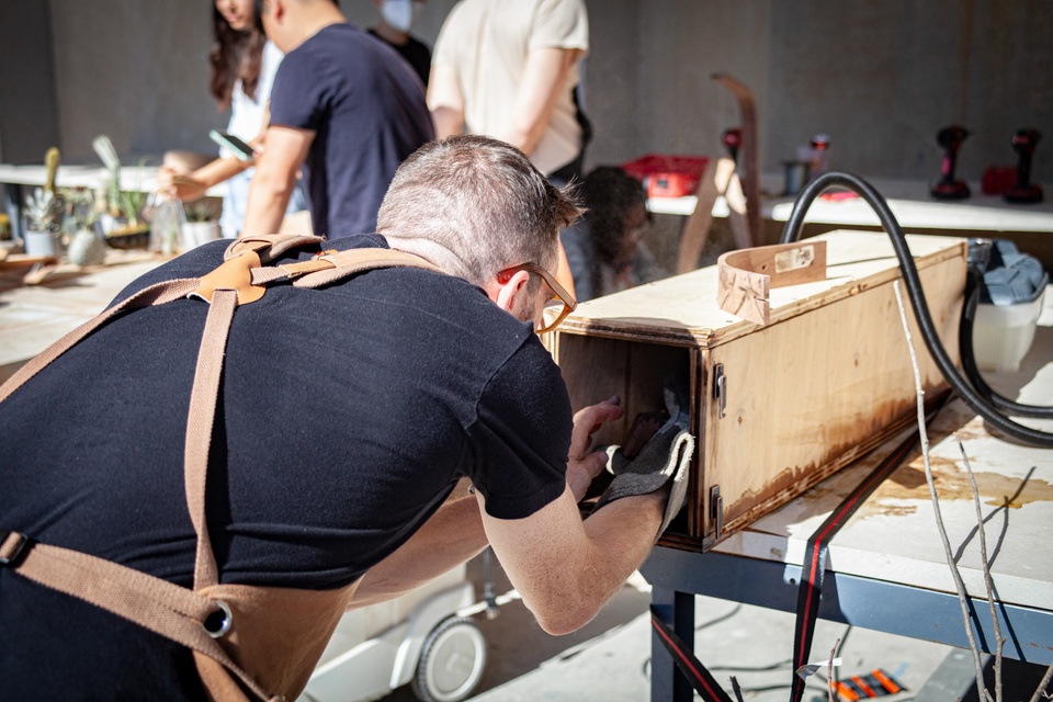 Greg Cuddihee places a piece of long wood into a steam rectangular wood container 