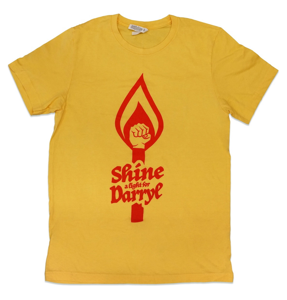 A yellow t-shirt with red graphic image of a fist inside a flame and the words “Shine a Light for Darryl Mount” underneath.