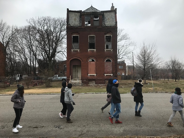 A group of people walk down a street in front of an empty brick building. 