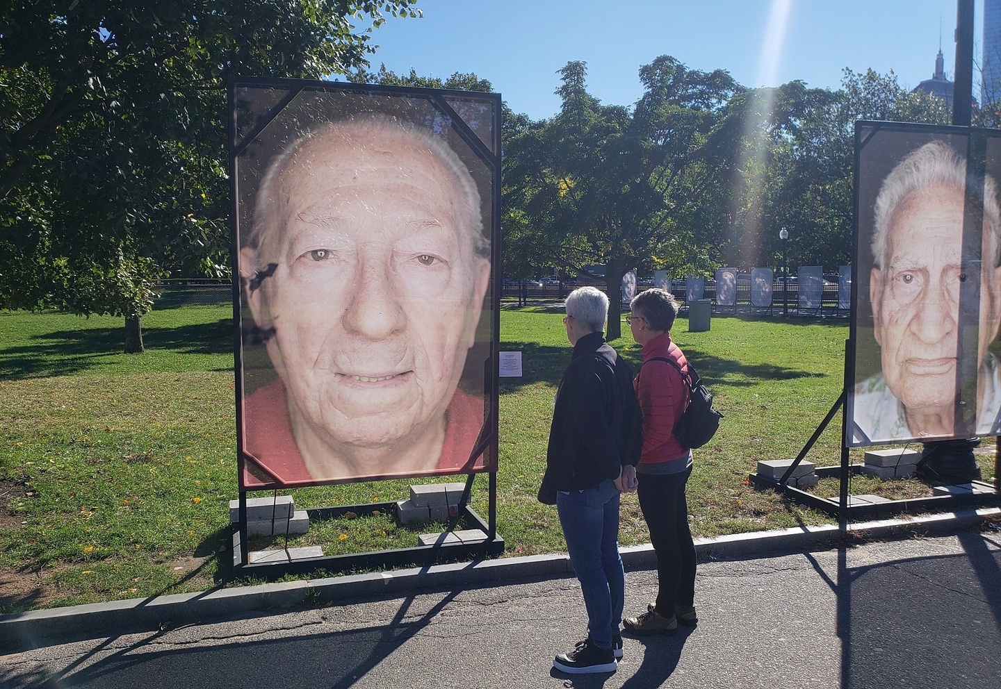 People in a park looking at large photographic portraits of older men