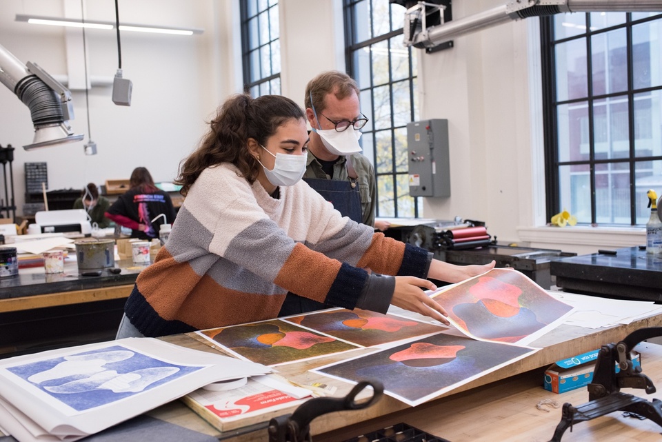 Person lays out multiple abstract prints in blue, red, and black to review with an instructor.