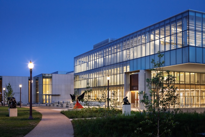 3-story glass walled building and a cantilever on one corner. Walkways wind by and a bright red Calder sculpture sits on the patio outside.