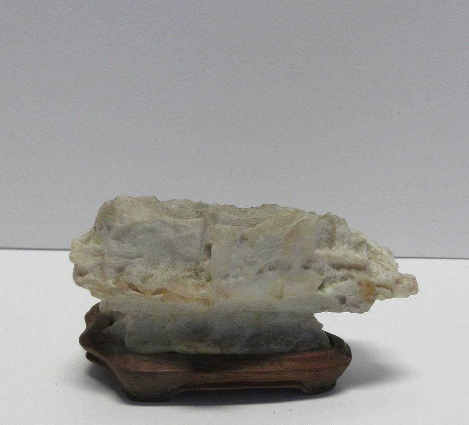 A light rough gray naturally formed stone, flat and rectangular shaped, sits atop a dark brown wooden base.
