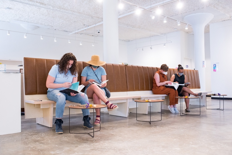 Four people sit on a row of benches and flip through a set of matching books.