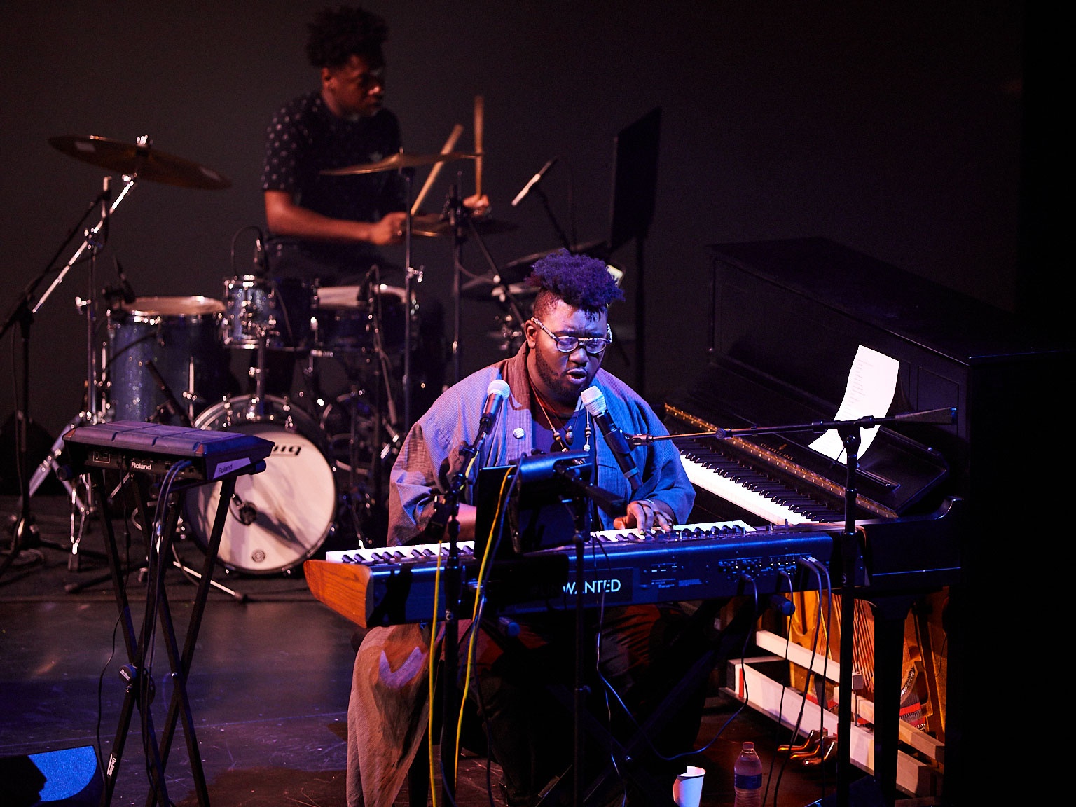 Tariq playing piano while singing on blue-lit stage.