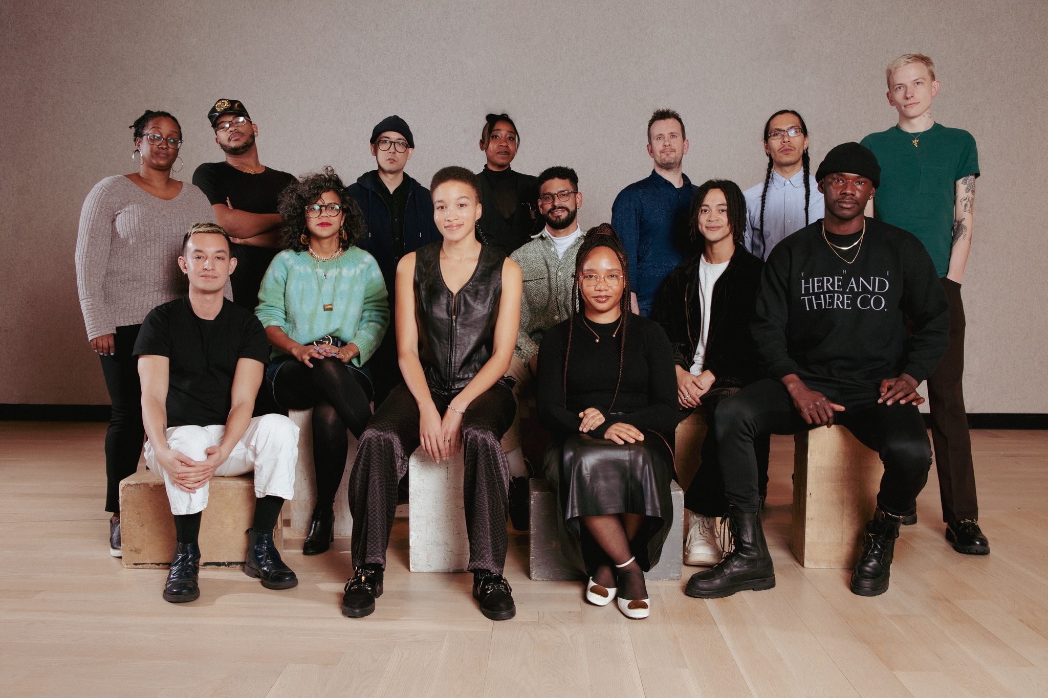A group photo of the 2023 and 2024 Open Call artists. The artists are arranged class photo style in two rows, with one row in the back standing and the other seated in front.