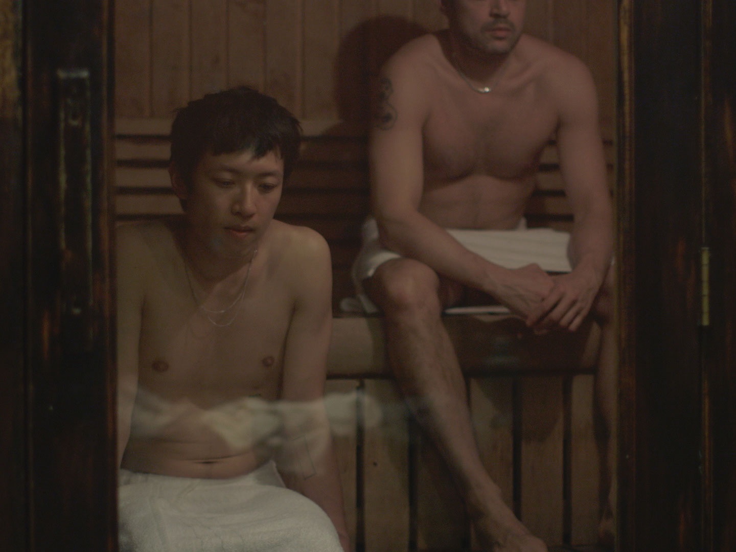 Two men in towels in a sauna.