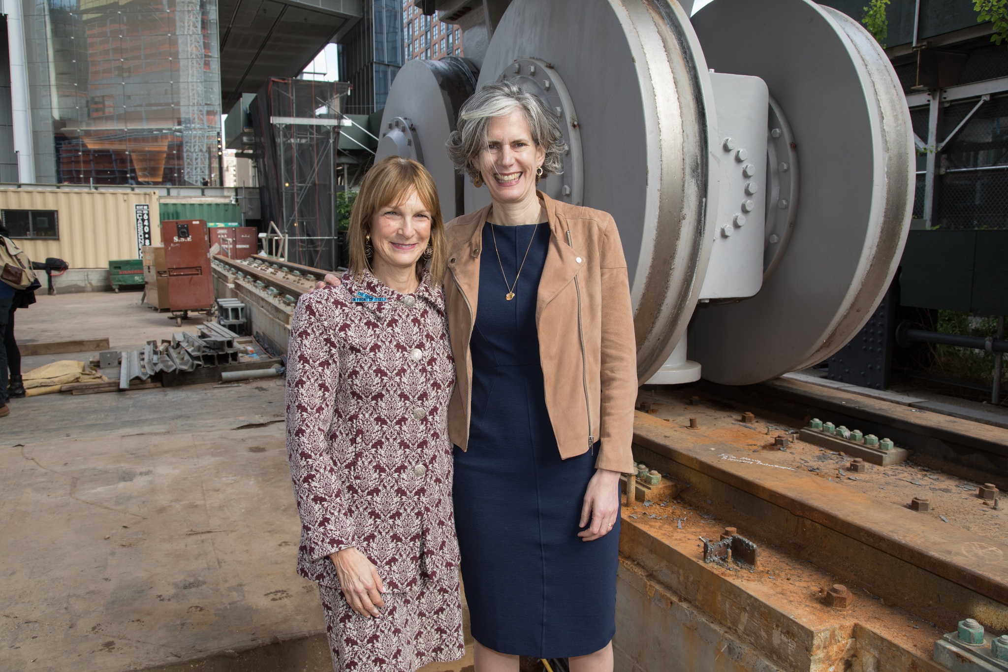 A photo of Bloomberg Philanthropies' Patti Harris and Kate Levin standing in front of The Shed's bogie wheels at The Shed's First Reveal in May 2017