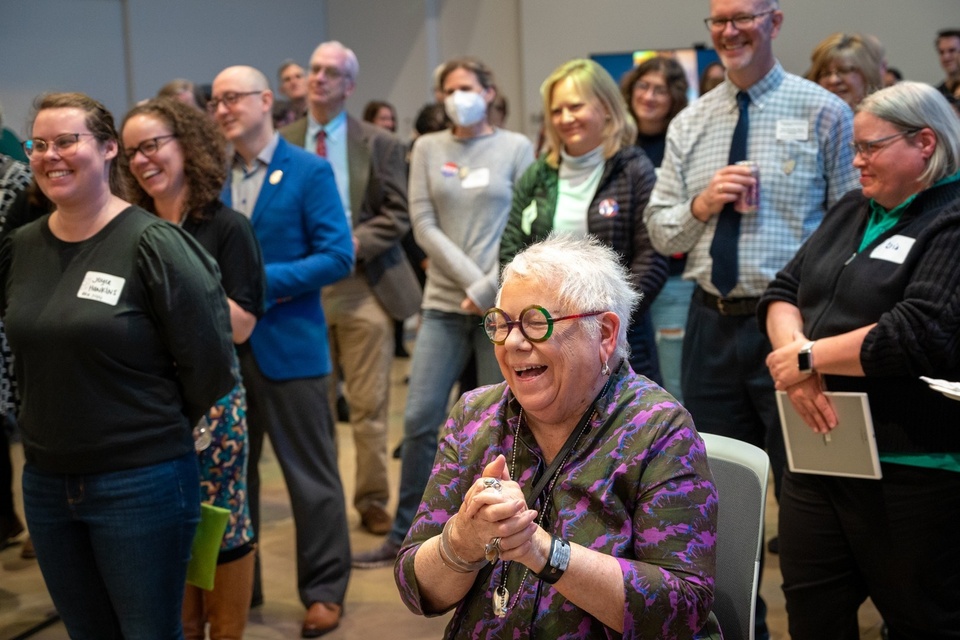 Georgia Binnington, seated at the front of a smiling crowd, laughs and claps her hands.