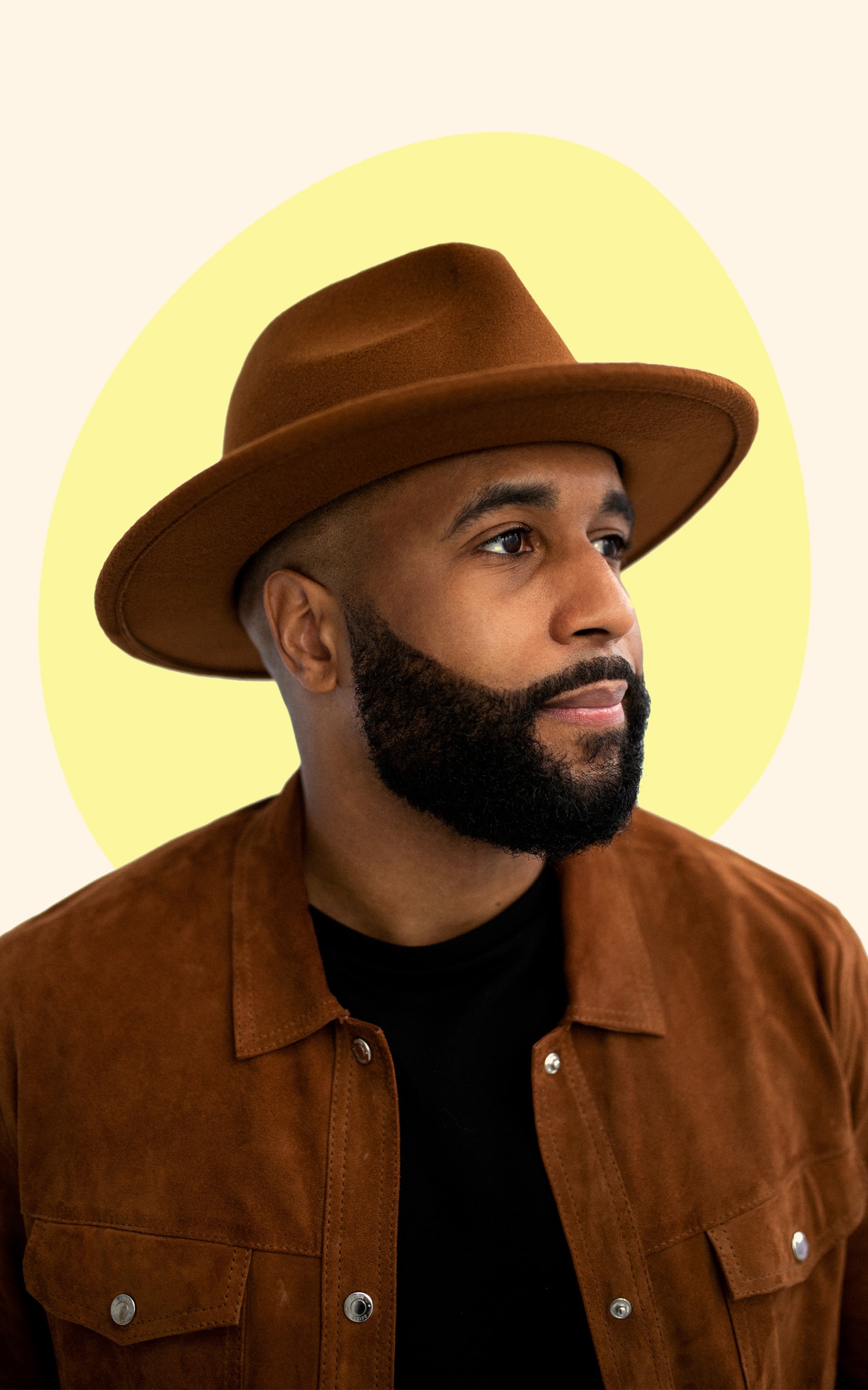 A Black man with a beard and mustache wearing a brown suede shirt and brimmed hat. The background behind him gives the effect of a yellow halo behind his head. 