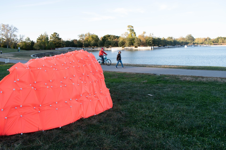 Pinkish-orange tent structure built on the grass in Forest Park, overlooking the water.