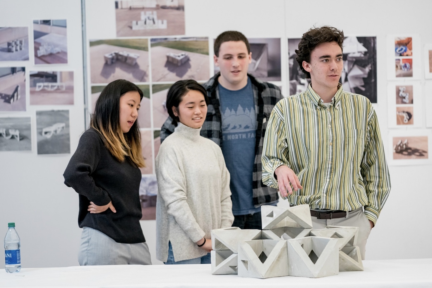 Four students stand behind the light-modulating, cast-concrete wall model they created; architerctural renderings are pinned on the wall behind them. 