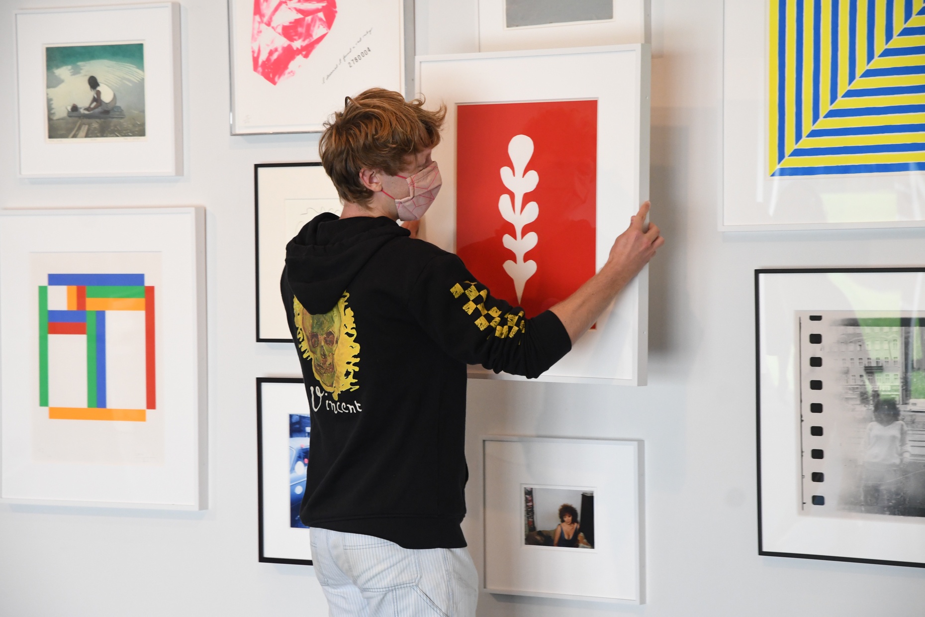 A student with their back towards us uses both hands to take a framed artwork by the artist Matisse off the wall.