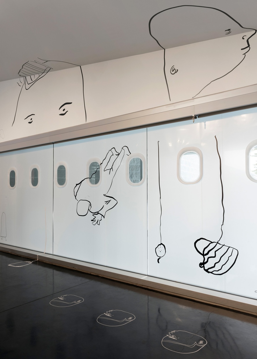 Seen at an angle, a large window and surrounding white wall and ceiling feature black line drawings, mostly of figures, and smaller white drawings on the black floor.