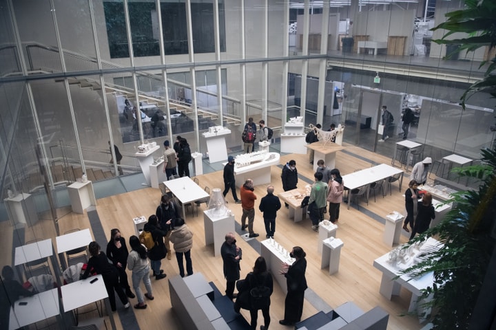 Overhead view of an interior courtyard space filled with architectural models on plinths with about 30 people milling around.
