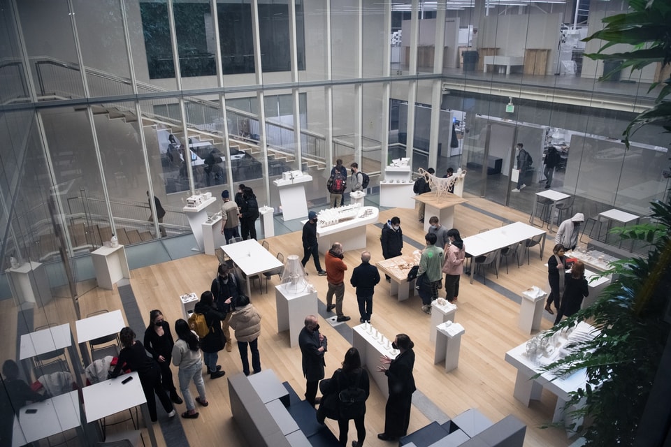 Overhead view of an interior courtyard space filled with architectural models on plinths with about 30 people milling around.