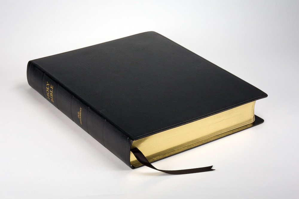 A black leather-bound book with gilded page edges and “HOLY BIBLE” and “OLD TESTAMENT” gilded on its spine.