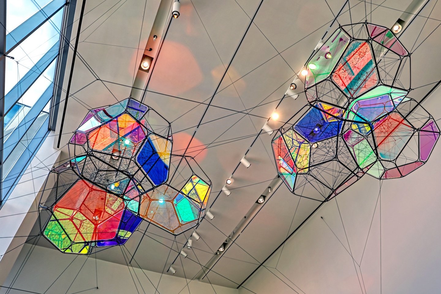 An iridescent, modular sculpture hanging from the ceiling with a system of ropes