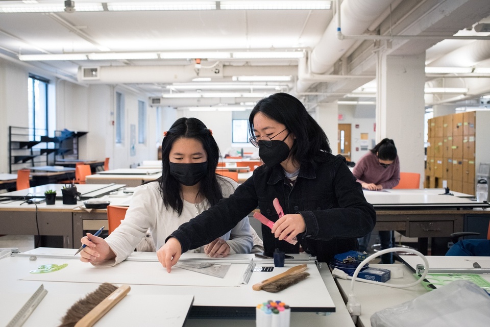 Two people discuss a drawing on a drafting board together.