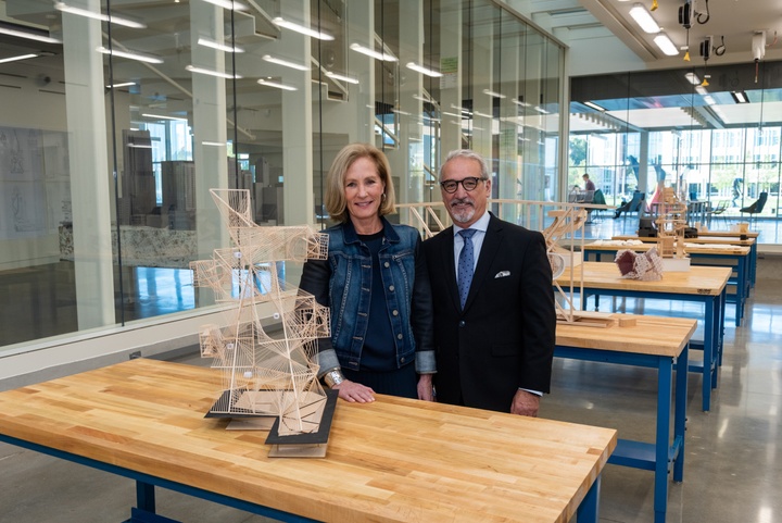 Two people pose by worktables covered in architectural models in a makerspace.