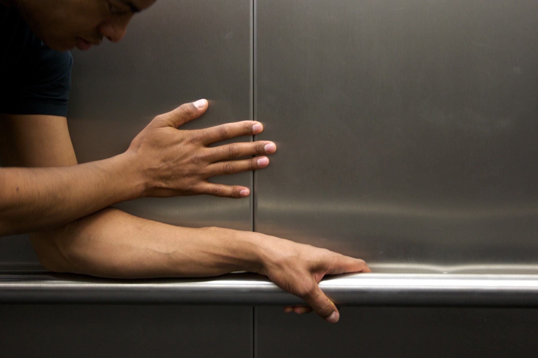 A tanned man holds onto a silver bar and feels his way along a metal wall.