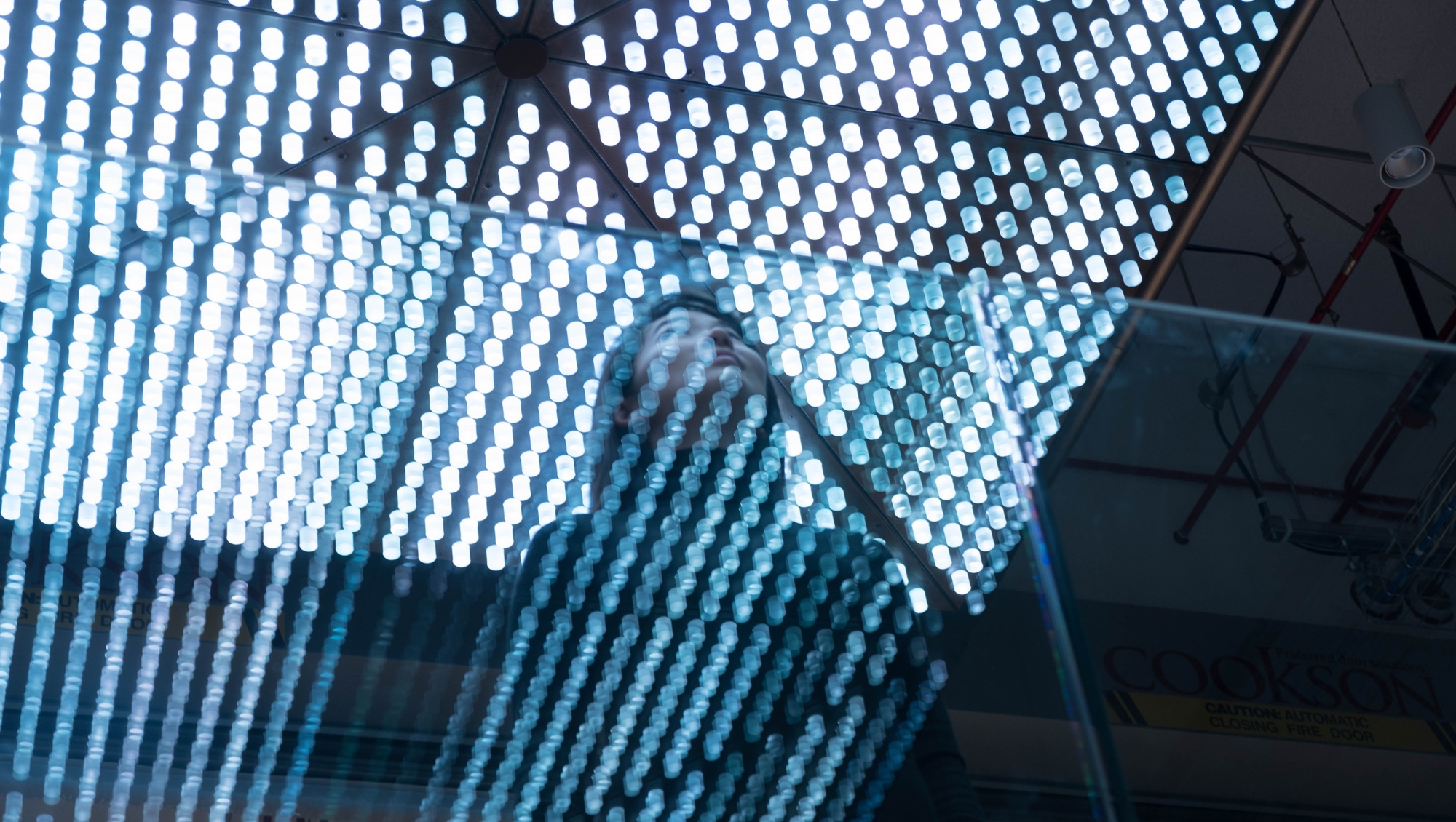 Woman looking up a illuminated surface made of many tiny lights in a grid pattern
