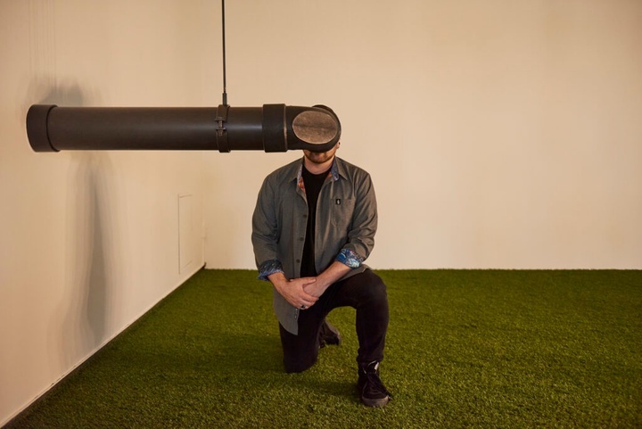 A person kneels on one knee looking into a periscope attached to the wall