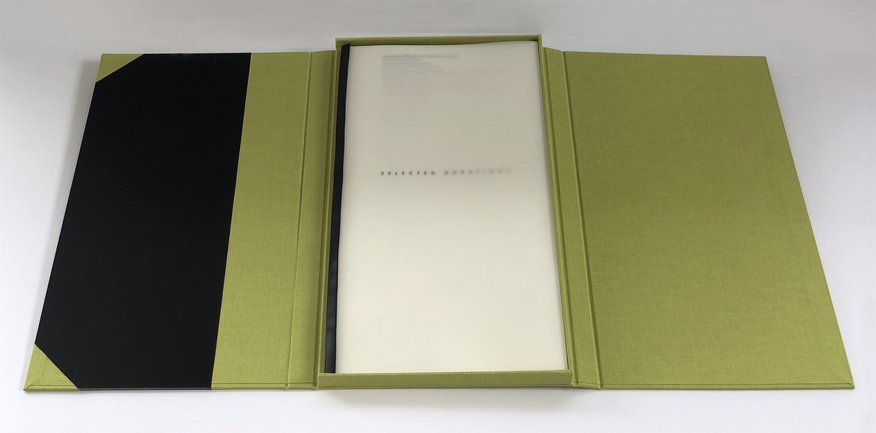 Letter press book opened up and lying flat; it has a black-and-olive green cover, with a skinny set of cream pages in the middle.
