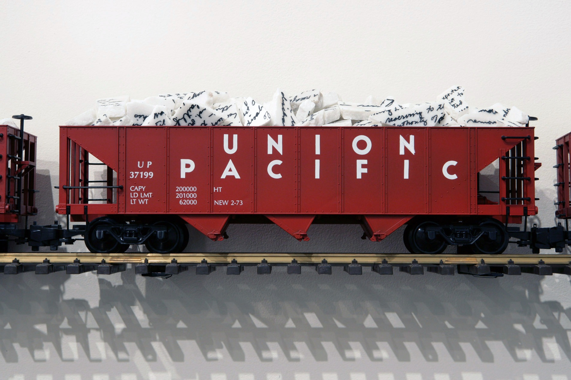 A red toy train with "Union Pacific" in white letters on the side rests on a small train track attached to a wall. The train has pieces of broken, white marble in it.