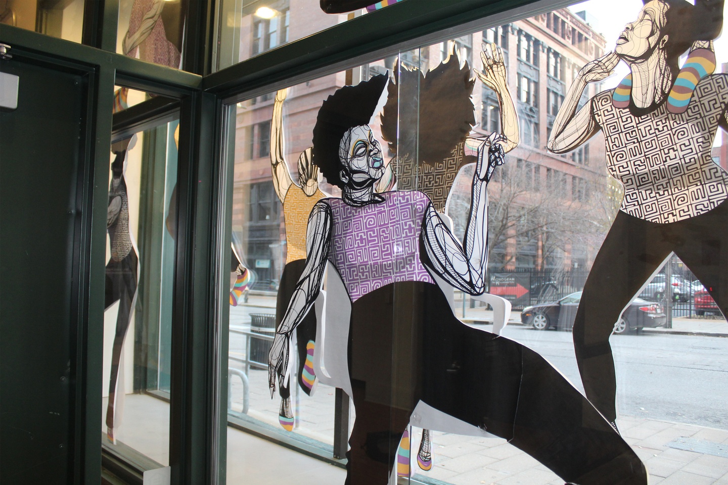 Large-scale paper cutouts of people in a window box with different patterns on their clothing, who appear to be dancing.