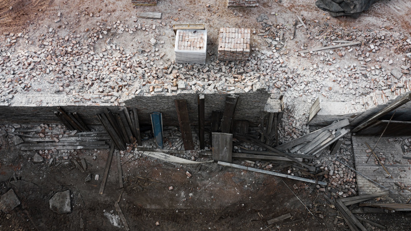 Drone photo of a dusty, demolished brick building with two stacks of bricks being made from the rubble.