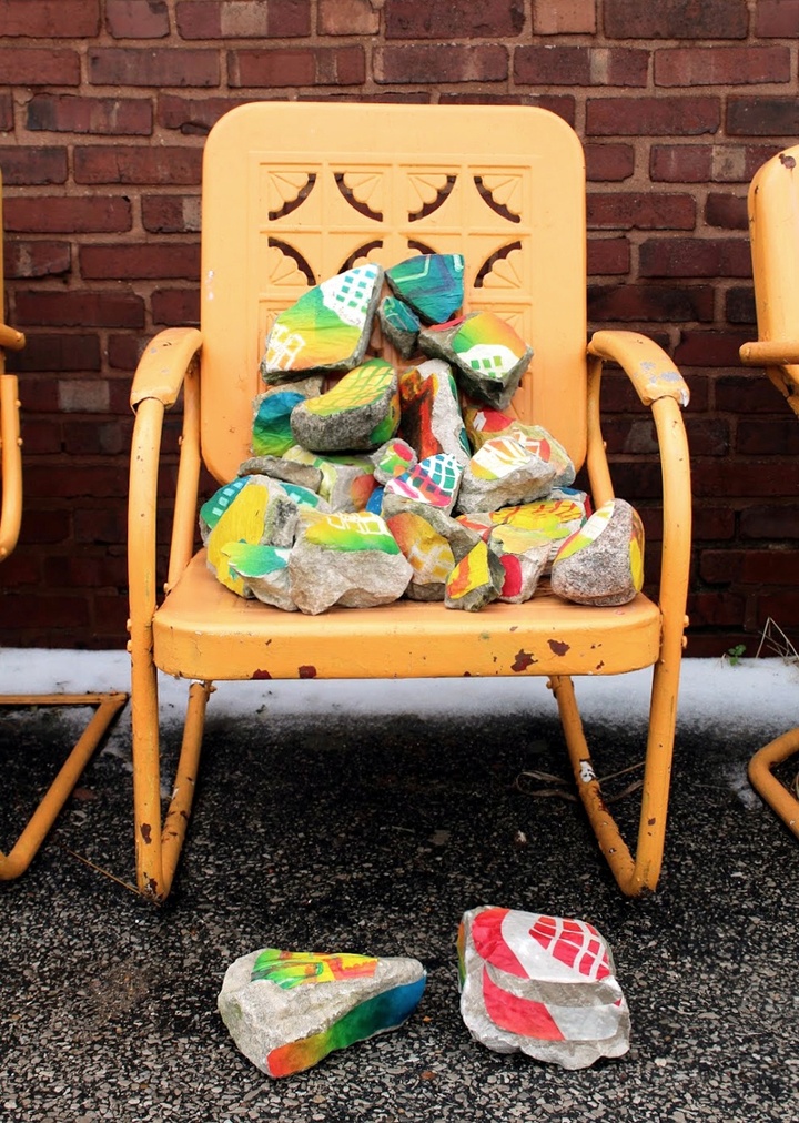 An orange chair with some colored rocks on the seat and two rocks on the ground in front of it