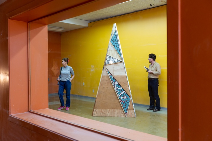 Looking through a orange window at a triangular larger-than-life sculpture shaped like a narrow pyramid
