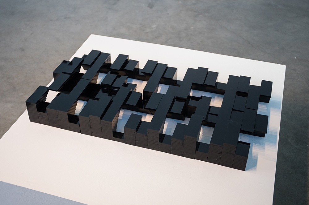 Three rows of black cuboids of different sizes and shapes interlocking, set on top of a white plinth.