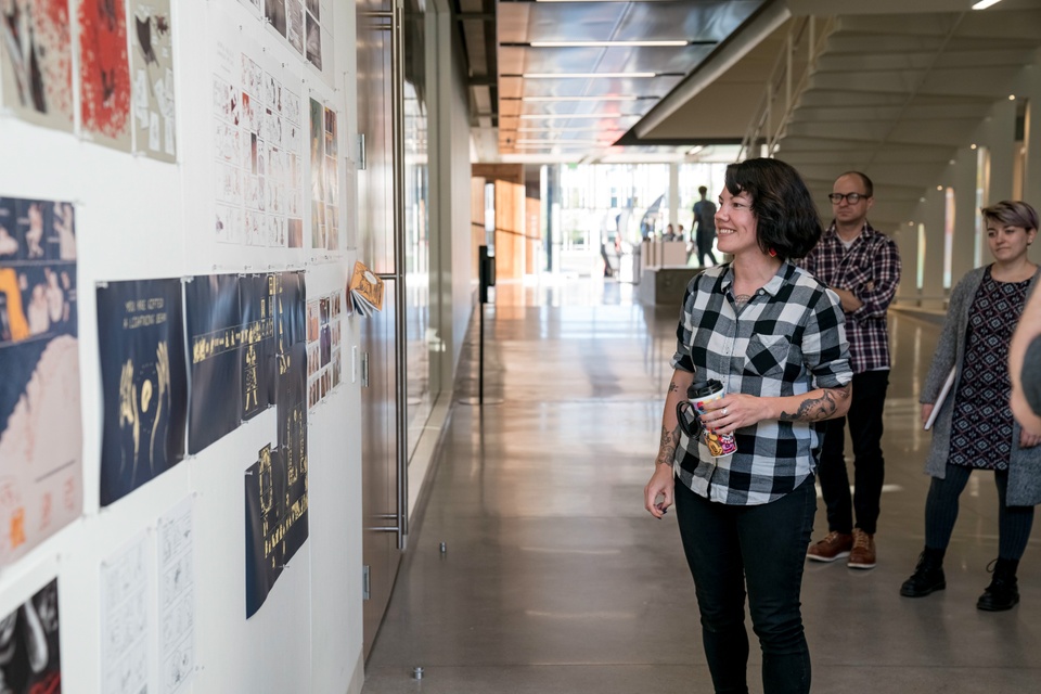 Person stands in an open walkway outside of studios looking at work on a large pin-up wall.