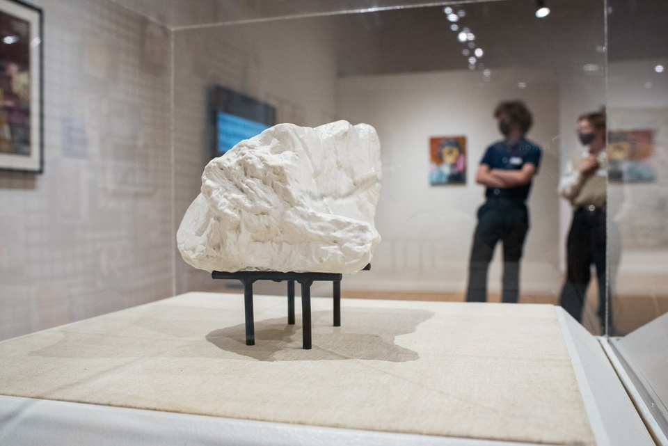 Close up of a white rock raised above a white canvas mat by a black base with stick legs.