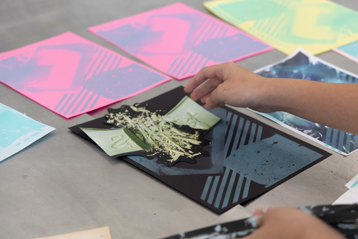 a hand placing items on a piece of paper to use as part of printmaking with several pieces of colorful paper on the table