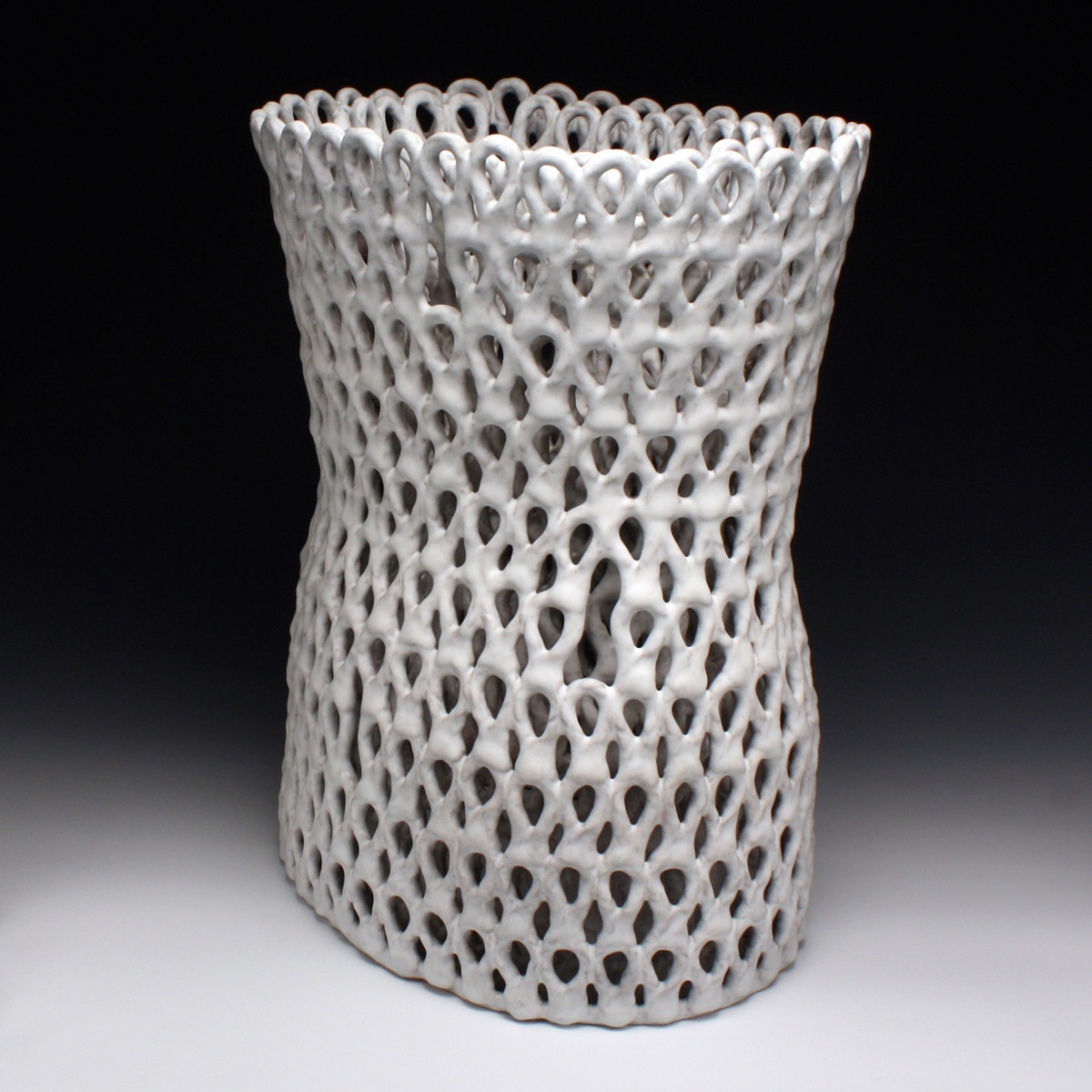 An intricately looped/patterned vessel in white, curved in at the middle, as if emerging from the shadows in the background.